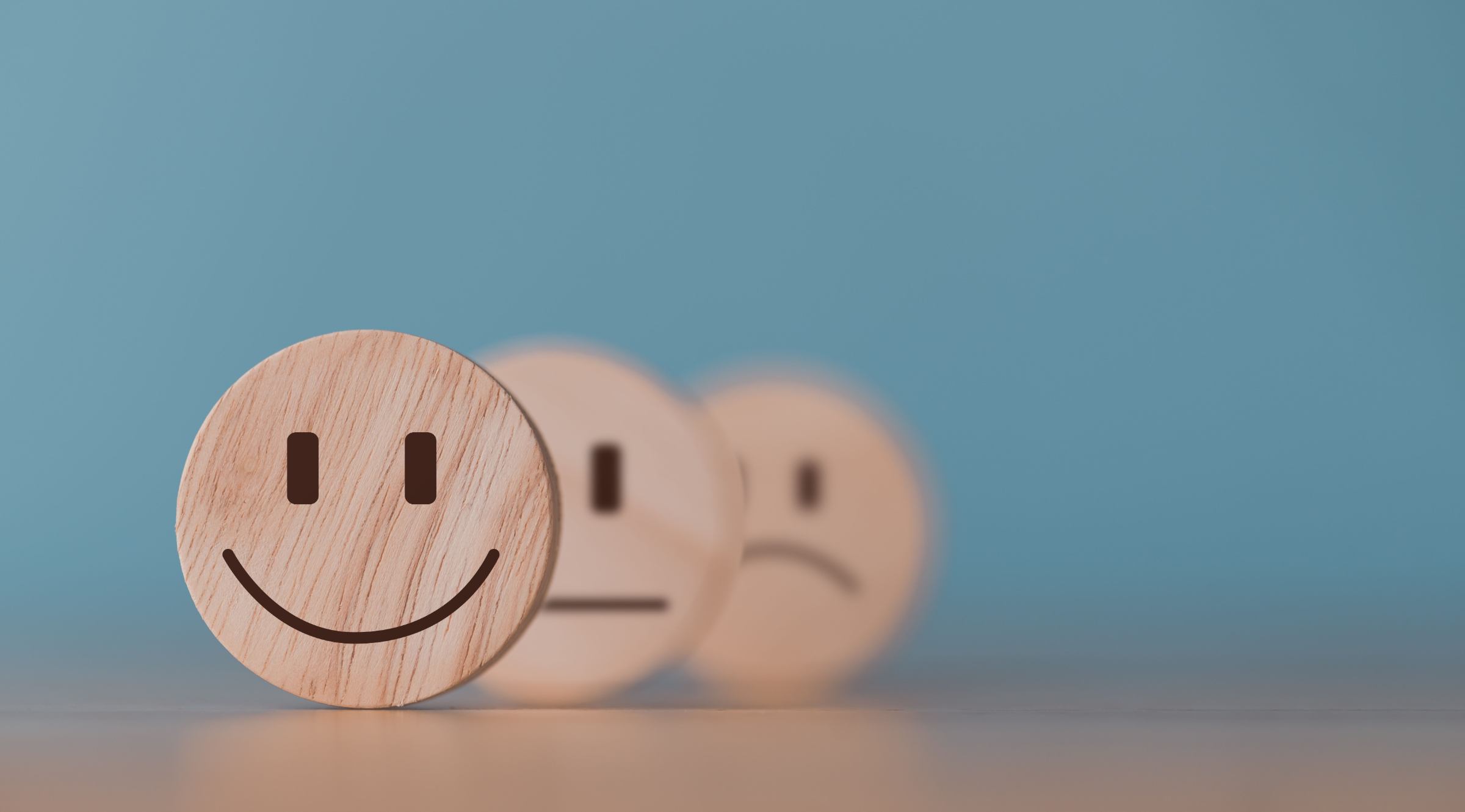 Een houten smileygezicht staat vooraan, gevolgd door een neutraal en een verdrietig gezicht, symboliserend de positieve ervaringen en klanttevredenheid bij hypnoQI in Willebroek.